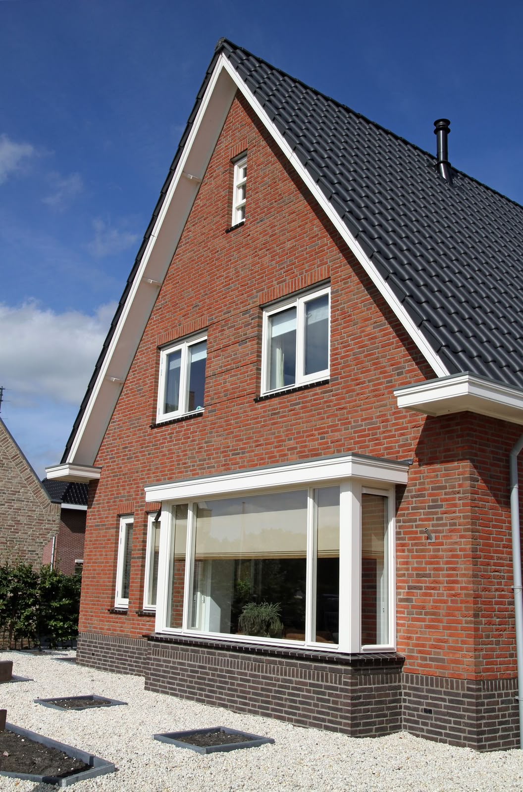 Wit geschilderde kozijnen, boeidelen en topgevel van een bakstenen woning