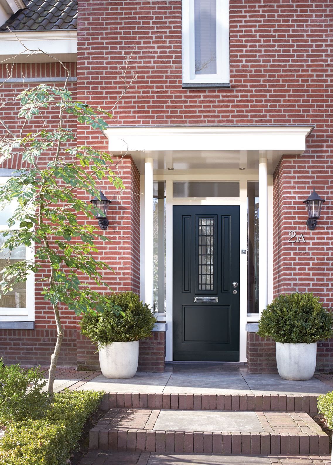 Donkergroen gelakte voordeur met witte omlijsting en luifel aan een bakstenen woning